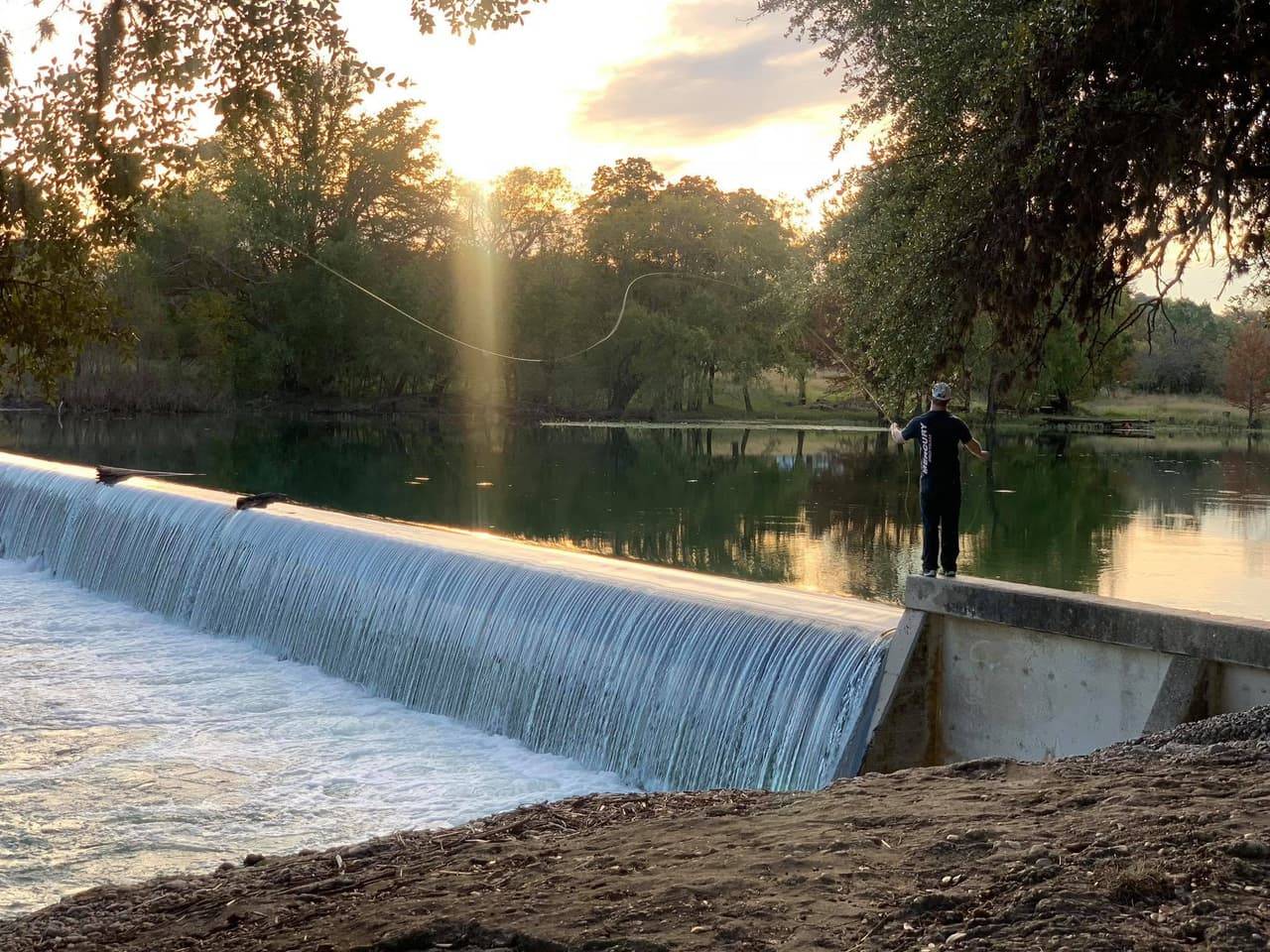 Angler fly-fishing at a low-water dam on the Sabinal River at golden-hour sunset