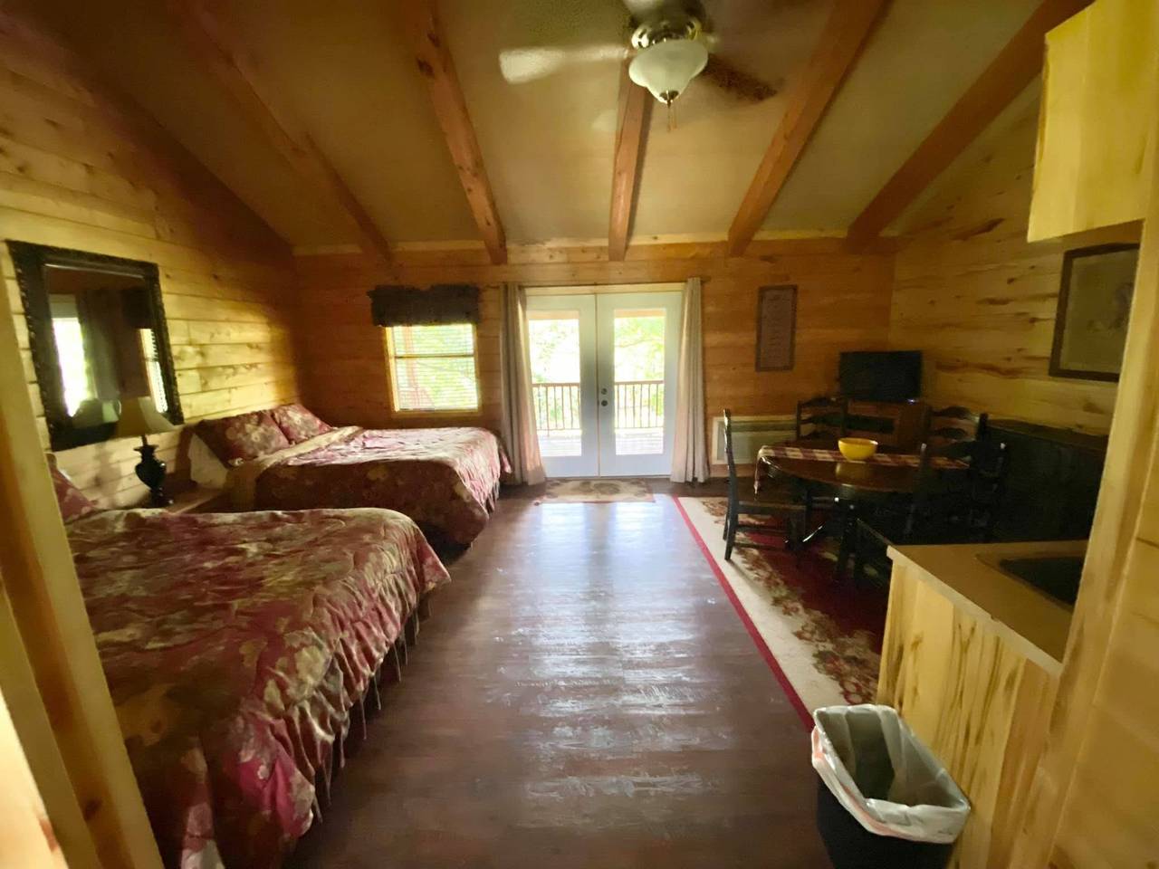Lodge bedroom with two floral-comforter beds, a kitchenette, and mounted TV at Sabinal River Lodge