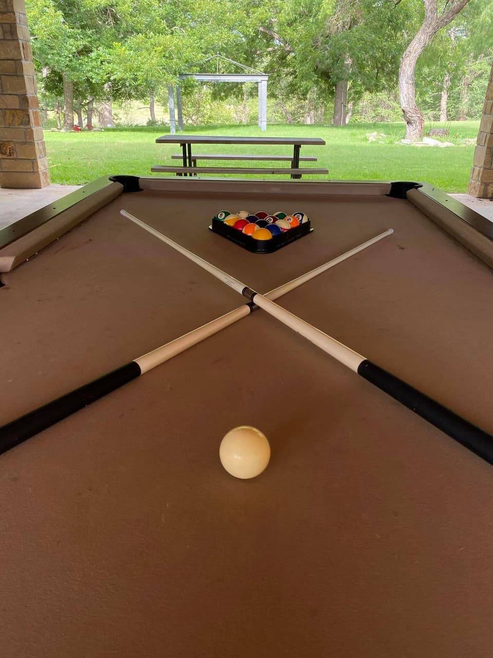 Covered pool table area at Sabinal River Lodge overlooking a grassy lawn and pergola