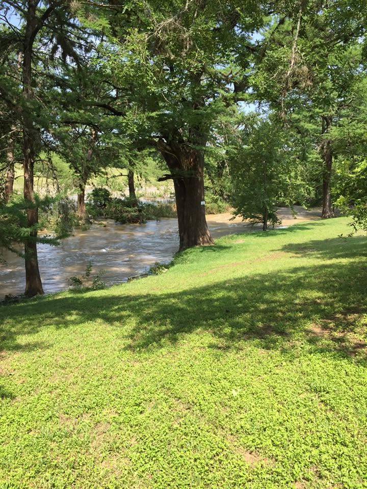 Grassy riverbank lawn and shaded path along the Sabinal River at Sabinal River Lodge