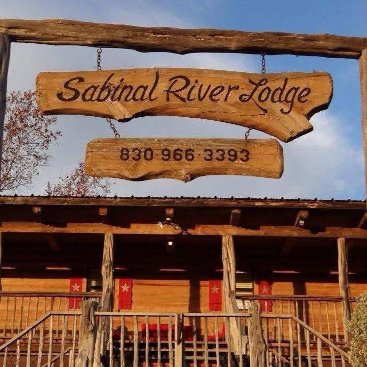 Wooden Sabinal River Lodge entrance sign with phone number 830-966-3393 hanging above the lodge porch in Utopia, Texas