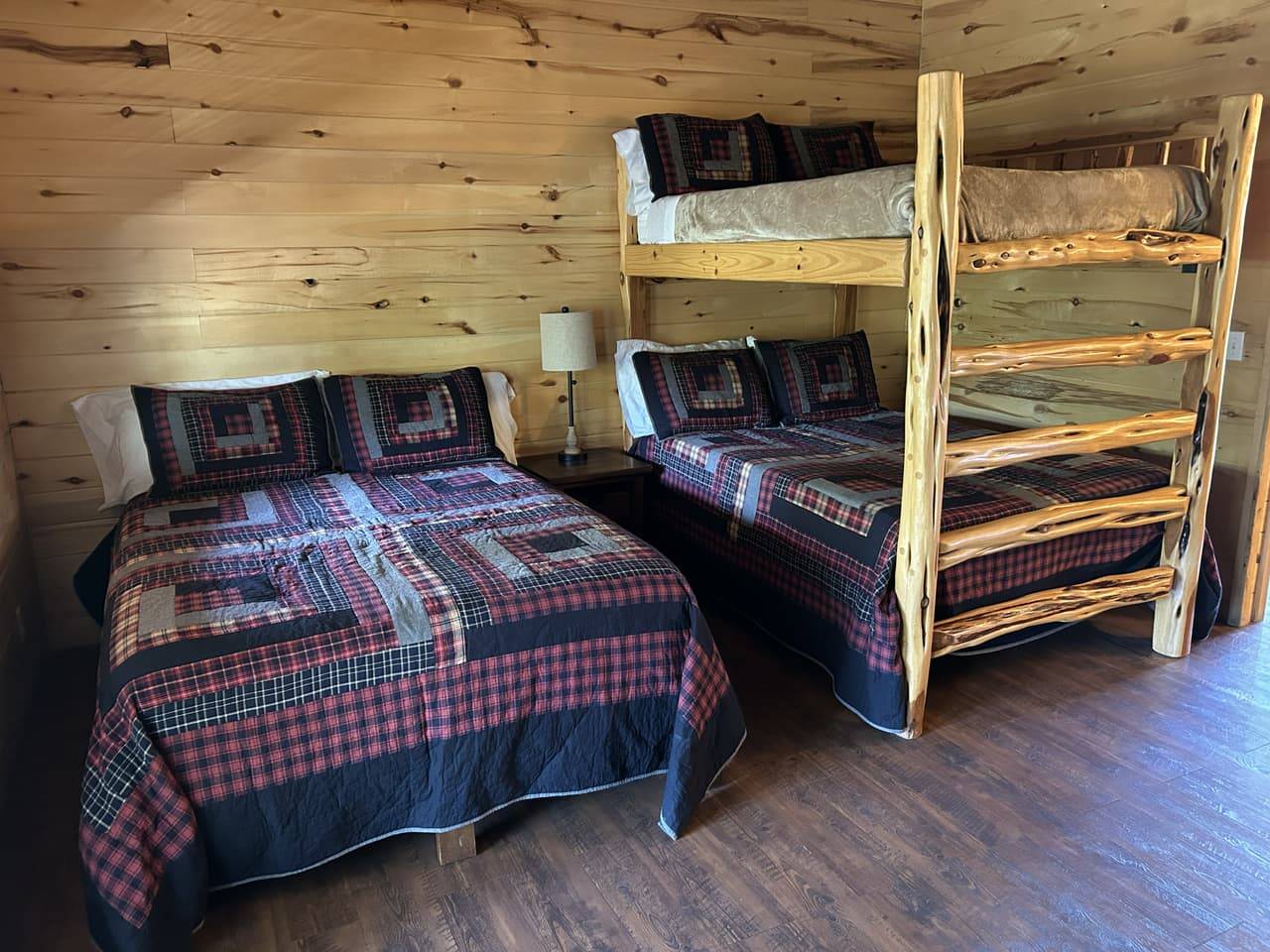 Family Suite bedroom at Sabinal River Lodge in Utopia, Texas, with a queen bed and log bunk bed dressed in plaid quilts
