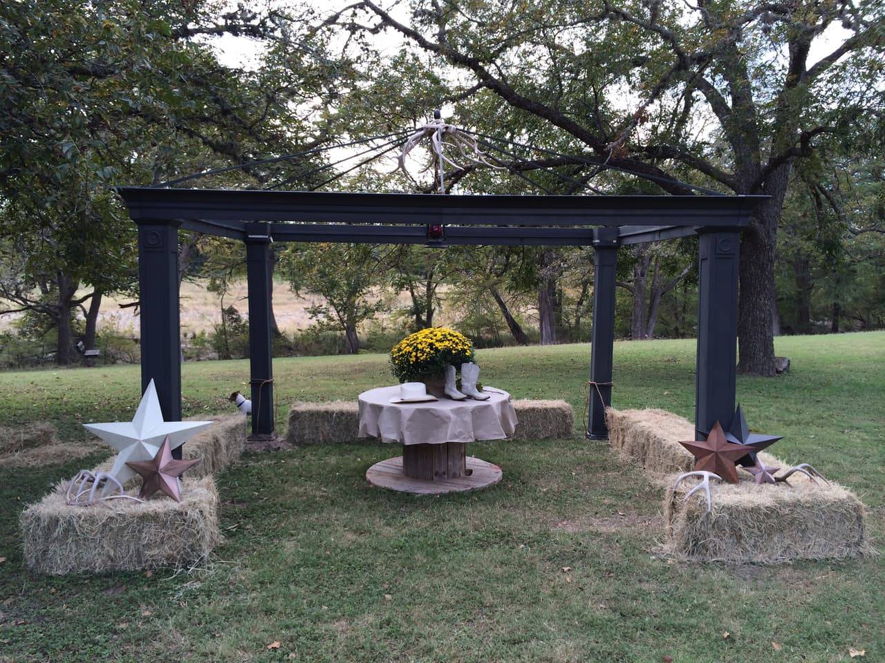 Dark metal reception pergola with an antler chandelier, cowboy boots and hat centerpiece, and Texas star hay bale seating at Sabinal River Lodge