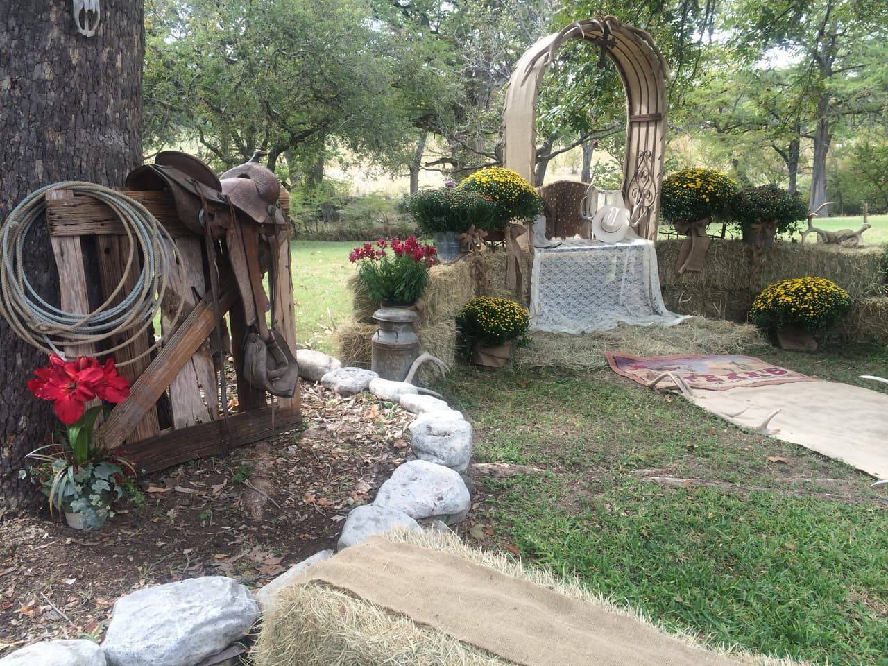 Rustic wedding ceremony arch decorated with a lasso rope, leather saddle, mums, and hay bales at Sabinal River Lodge