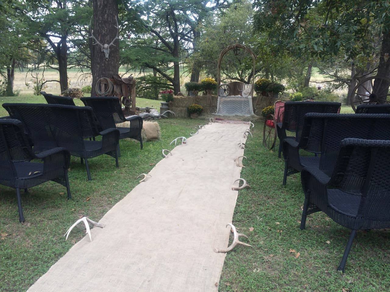 Wedding ceremony aisle with a burlap runner, antler markers, and black wicker guest chairs at Sabinal River Lodge