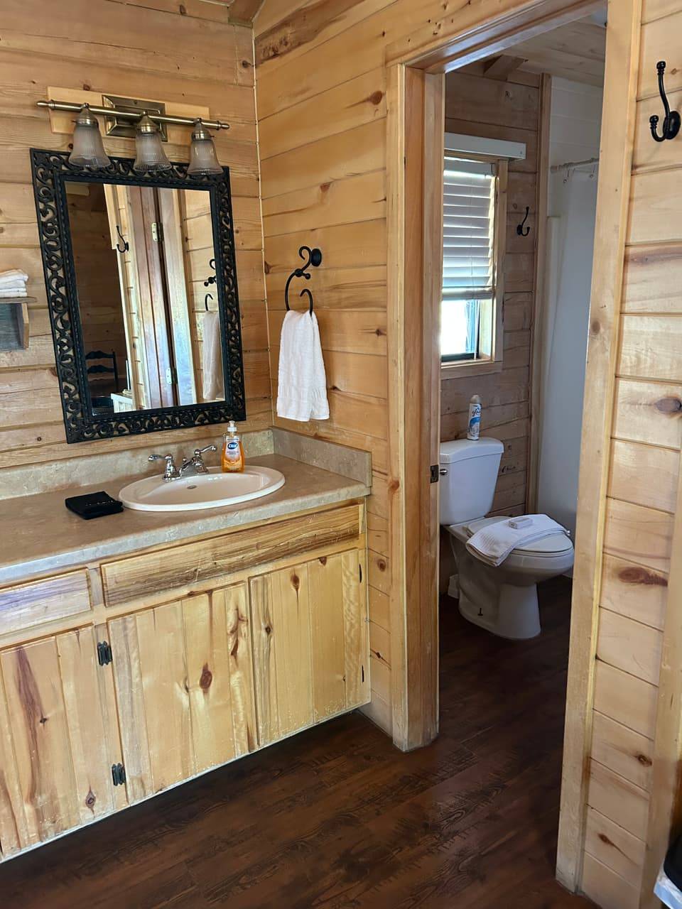 Private bathroom at Sabinal River Lodge in Utopia, Texas, with a knotty-pine vanity, mirror, and view through to the toilet and shower